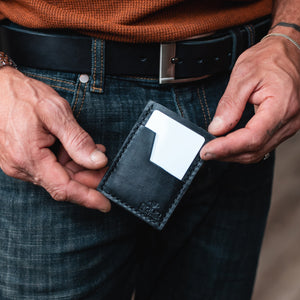 a mans hands holding a black leather cardholder wallet handmade by Solid Leather in Peterborough Ontario Canada, with a matching full grain leather belt worn on a pair of jeans