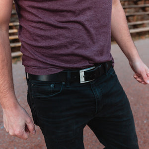 Solid Leather Casual black leather belt on a pair of black jeans with tucked in t-shirt with a warm blurred background