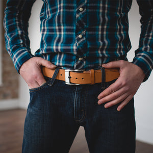 a full grain leather belt in natural tan with stainless steel buckle worn on blue jeans with a plaid shirt tucked in
