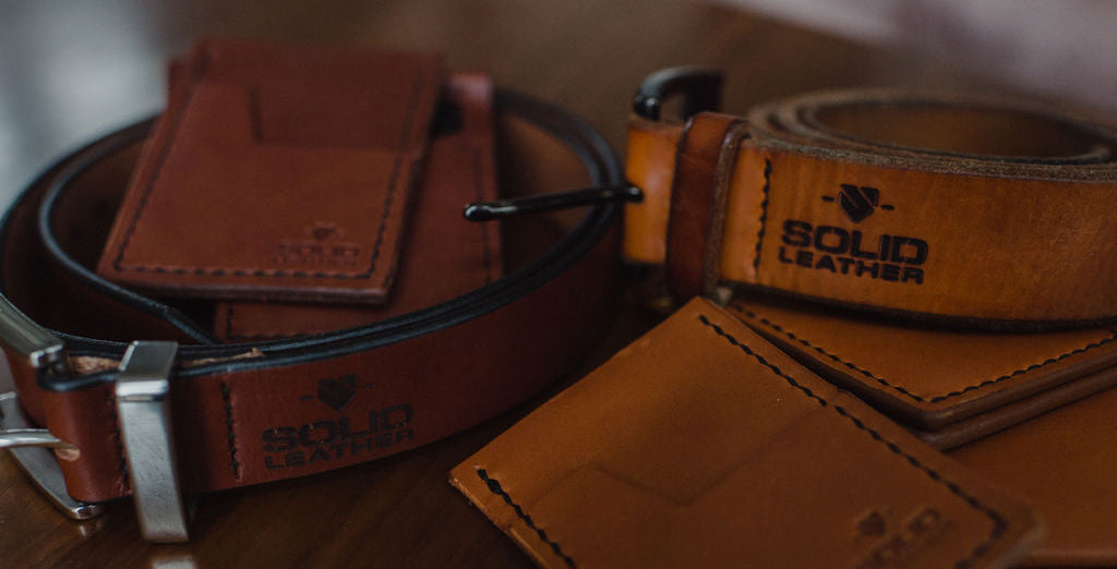 Two brown leather belts with matching leather wallets xs, displayed on a wooden surface. One belt is a formal cognac brown leather with a stainless steel buckle, and the other is casual tan leather belt.