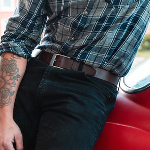 a man leans against a red car wearing a full grain Solid Leather belt in brown with dark jeans and a plaid shirt