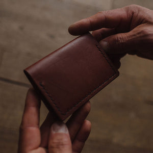 a pair of mans hands holding a solid leather cognac brown bifold cardholder wallet showing the front side on a blurred background