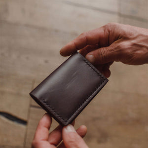 a dark brown leather bifold cardholder wallet held by a pair of hands on a warm blurred background