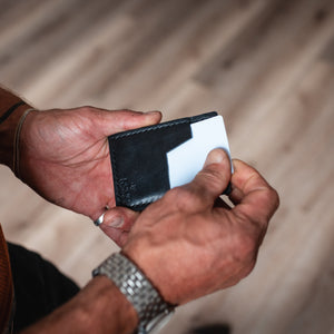 hands pulling a card out of a solid leather black slim cardholder wallet