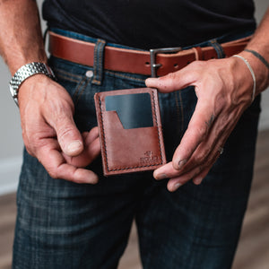 a mans hands holding a slim cardholder wallet handmade by jesse bateson of Solid Leather with a matching full grain leather belt in background on dark jeans and a black tshirt