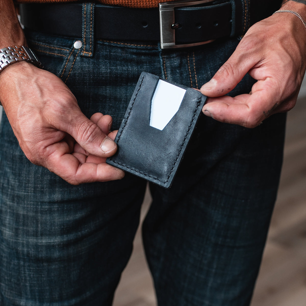 mans hands holding a black leather card holder wallet with a white card showing the back side 