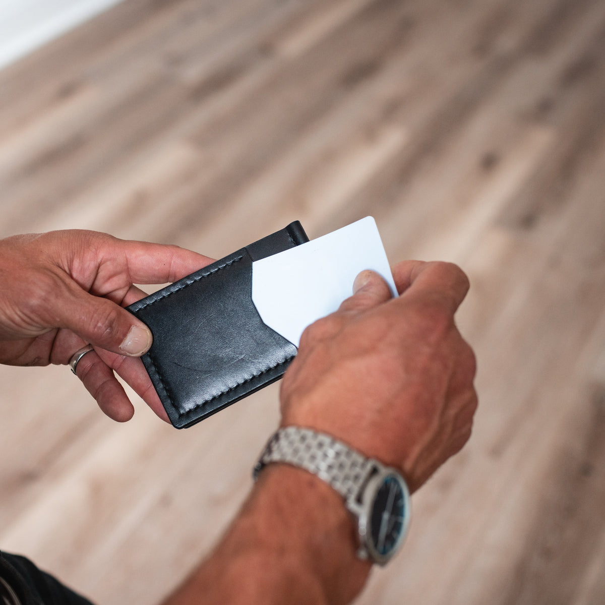 handmade black leather money clip wallet front side being held by two hands with a blurred background 