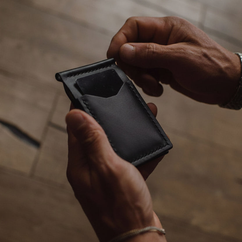 handmade black leather wallet being held by 2 hands with a blurred background. 