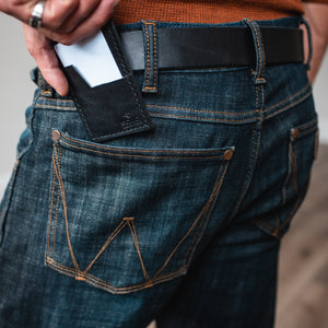 a black leather cardholder wallet, back pocket dark jeans with a matching full grain leather black belt 