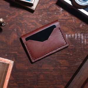 a cognac brown Solid Leather bifold cardholder wallet on a dark wooden desk. Handmade in Peterborough Ontario Canada by Jesse Bateson 