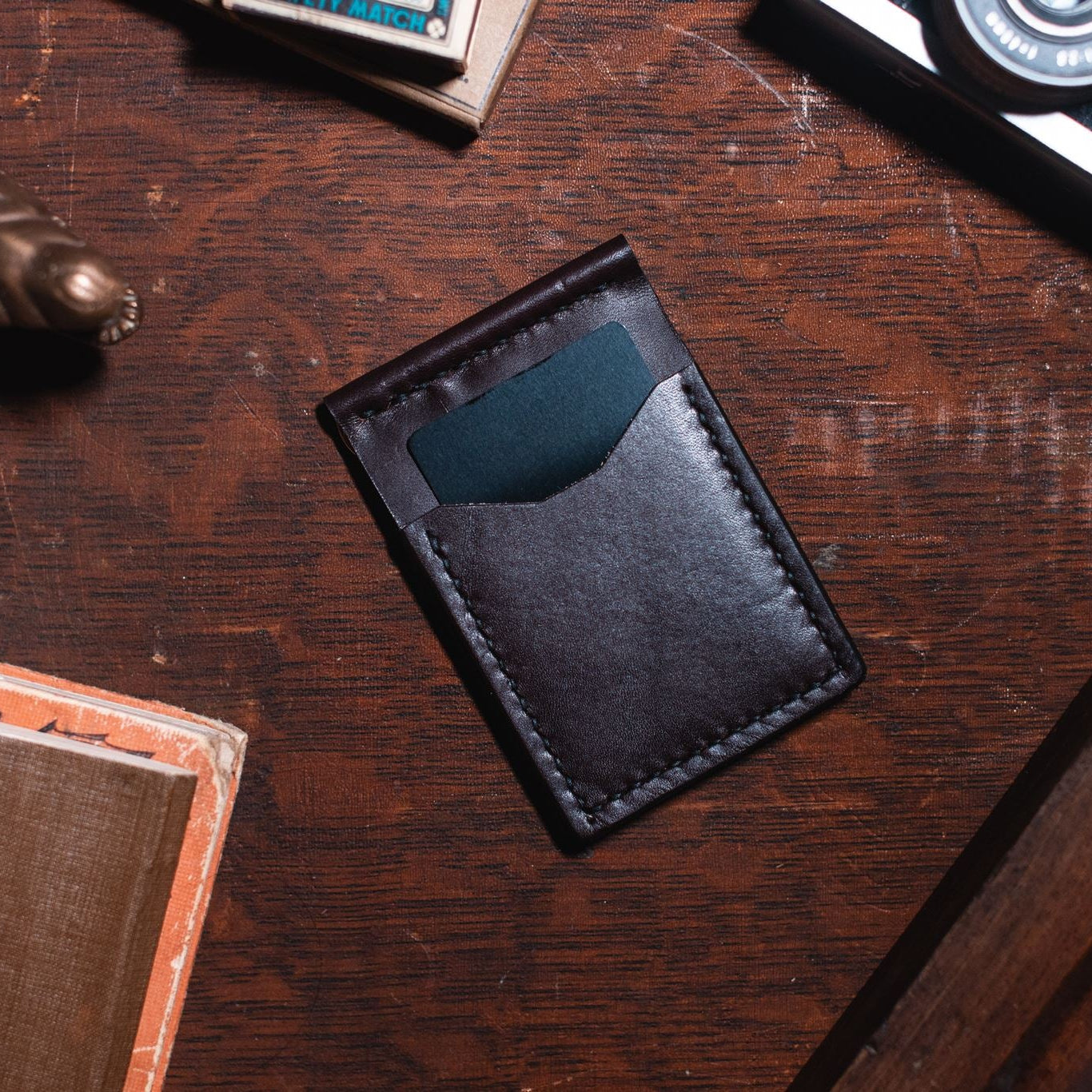 Solid Leather dark brown money clip cardholder wallet on a dark wooden desk 
