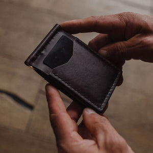 a dark brown leather cardholder wallet held by to hands with a blurry background.  