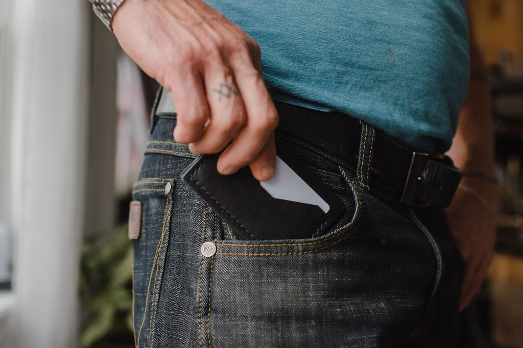 Solid Leather everyday minimalist bifold wallet coming out of a pair of dark jeans front pocket 