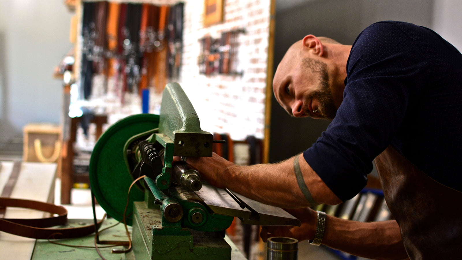 Jesse Bateson of Solid Leather  operating a green leather strap cutter in his Solid Leather workshop setting
