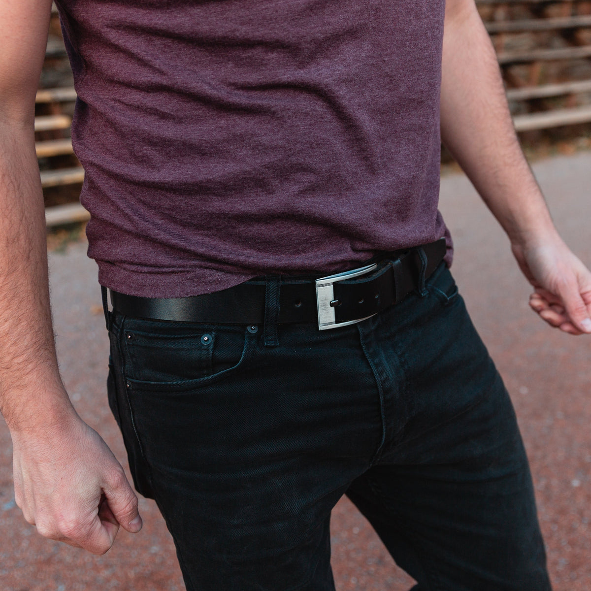 Solid Leather Casual black leather belt on a pair of black jeans with tucked in t-shirt with a warm blurred background 