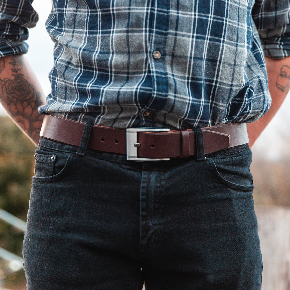 A full-grain leather belt in brown on a pair of dark jeasn with a tucked in plaid shirt 