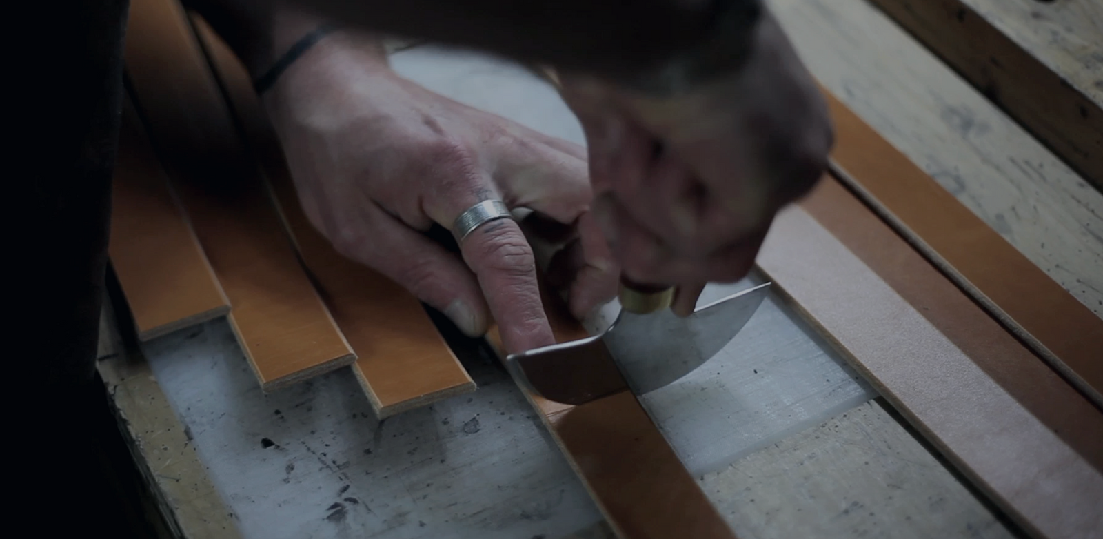 Jesse using a knife to cut a leather belt on his workbench 