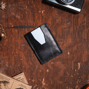 a slim black leather cardholder wallet on a wood desk with vintage props