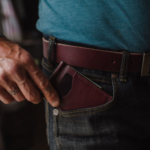 A close-up of a person wearing dark blue jeans and a teal t-shirt, showing a burgundy leather belt and matching leather money clip card holder wallet. Handmade in Peterborough Ontario by Solid Leather.