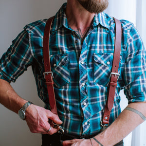 a pair of Solid Leather suspenders in cognac brown with stainless steel hardware over a teal plaid shirt 