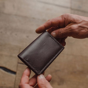 a dark brown leather bifold cardholder wallet held by a pair of hands on a warm blurred background 
