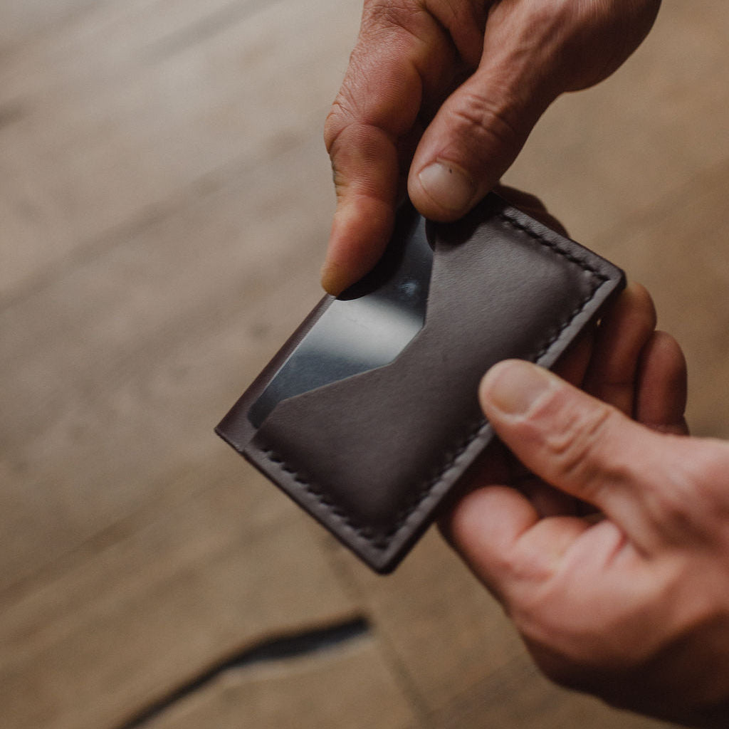 pair of hands showing the back pocket of a dark brown leather bifold cardholder wallet handmade by Solid Leather with blurred background 