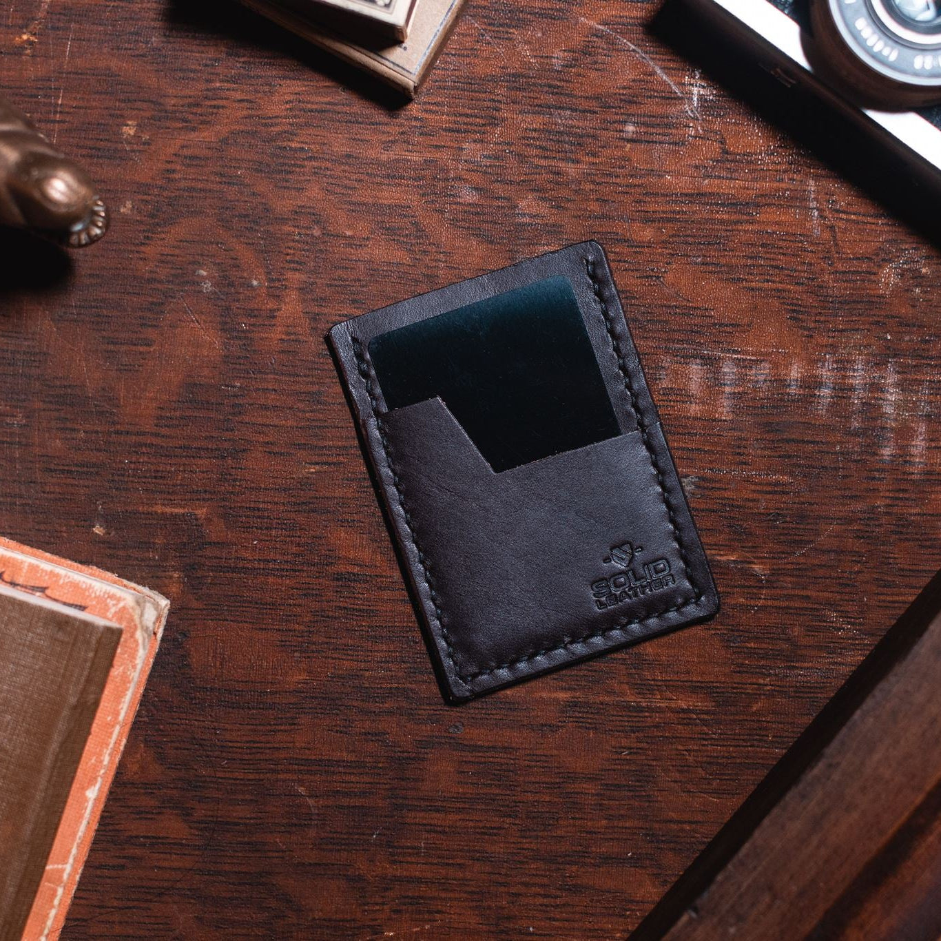 a slim Solid Leather dark brown cardholder wallet on a dark wood desk 