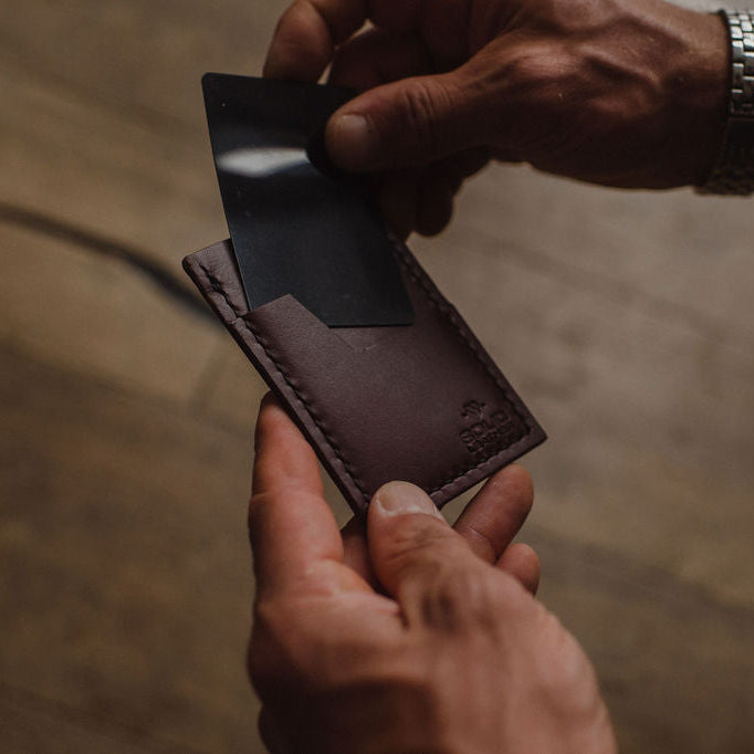 a mans hands removing a card from a Solid Leather slim wallet with blurred background