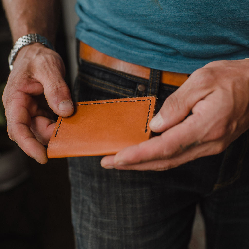 A pair of hands holding a Solid Leather tan bifold card wallet with matchng leather belt 