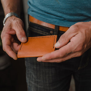 A pair of hands holding a Solid Leather tan bifold card wallet with matchng leather belt 