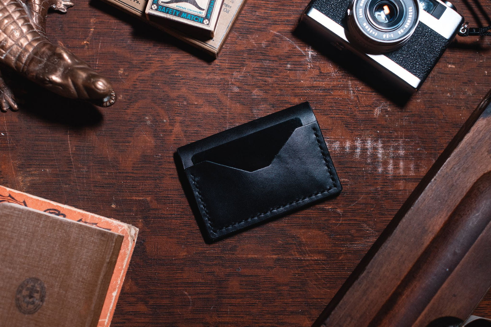 a black leather bifold wallet handmade by Solid Leather on a dark wooden desk 