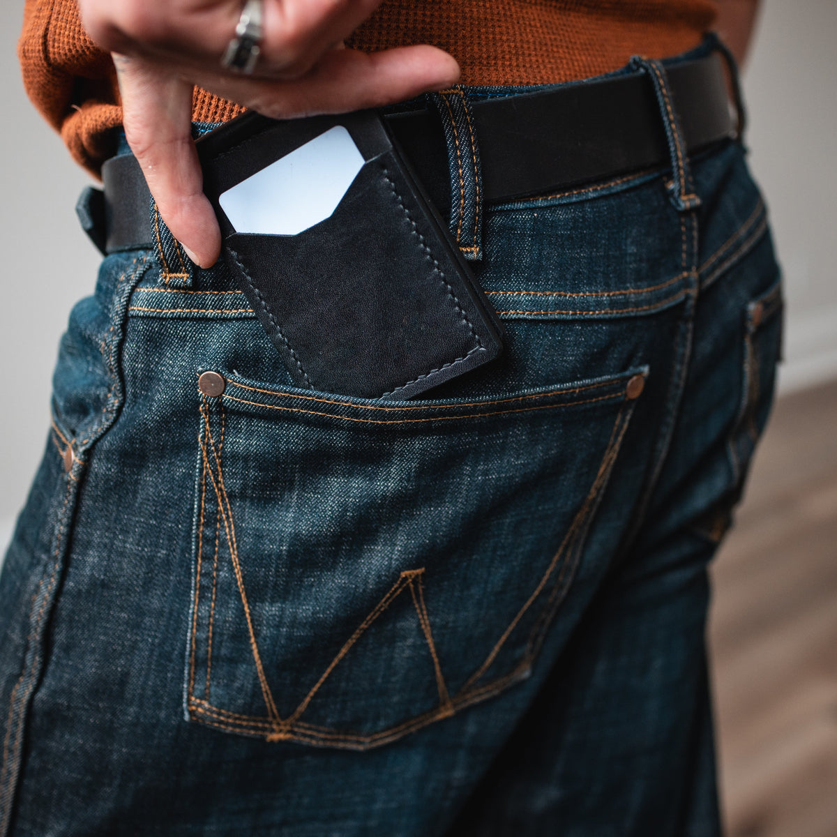 a black leather money clip wallet with matching full-grain leather belt worn on blue jeans. the leather money clip wallet is in the back pocket 