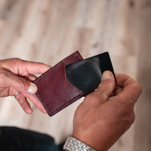 a burgundy leather cardholder wallet with money clip held by two hands pulling out a card 