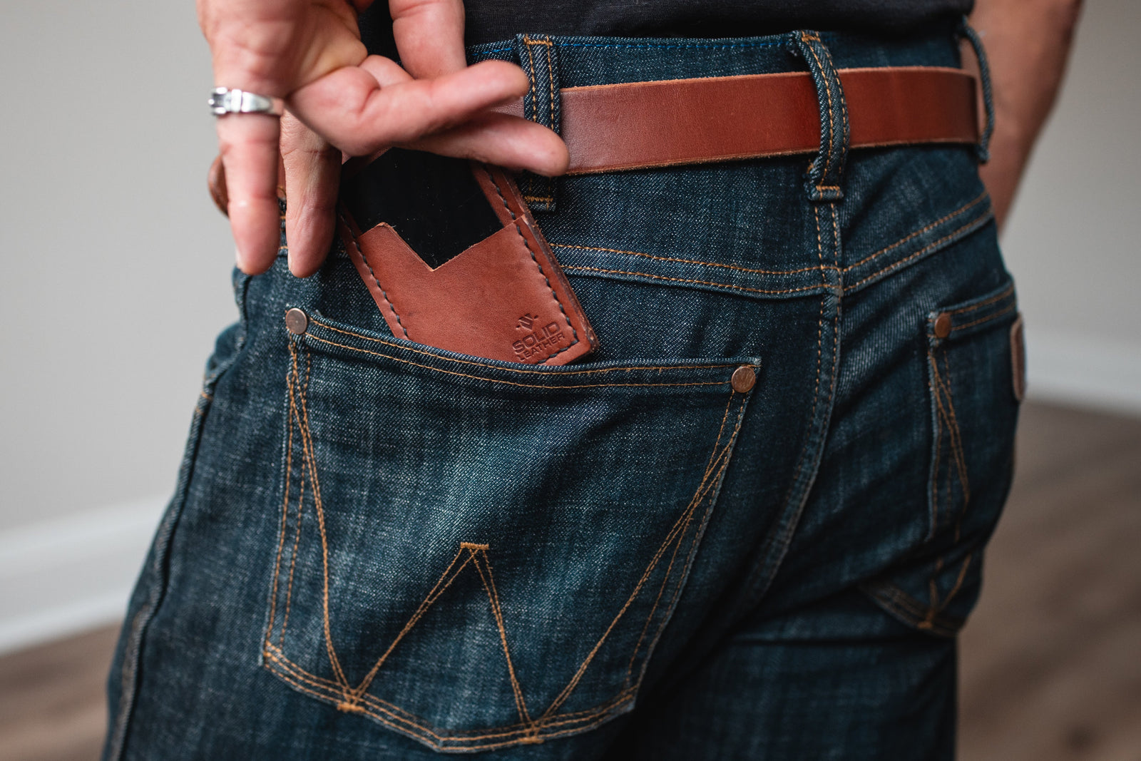 a cognac brown full-grain leather cardholder wallet with matching leather belt and a pair of blue jeans 