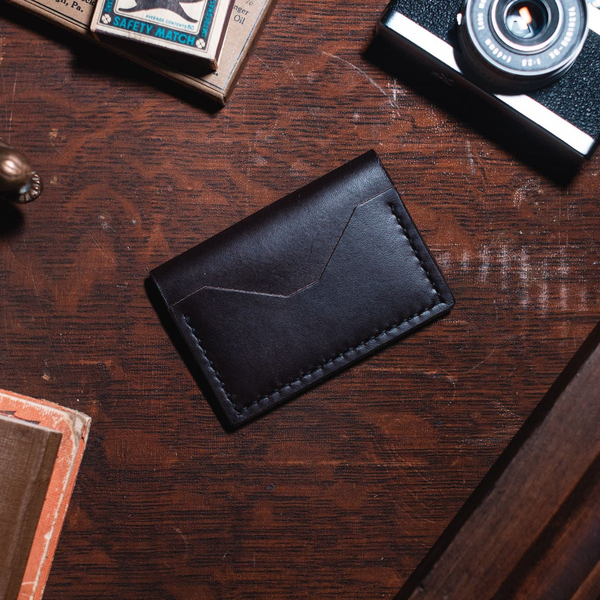 a dark brown leather bifold cardholder wallet on a dark wooden desk surrounded by vintage props 