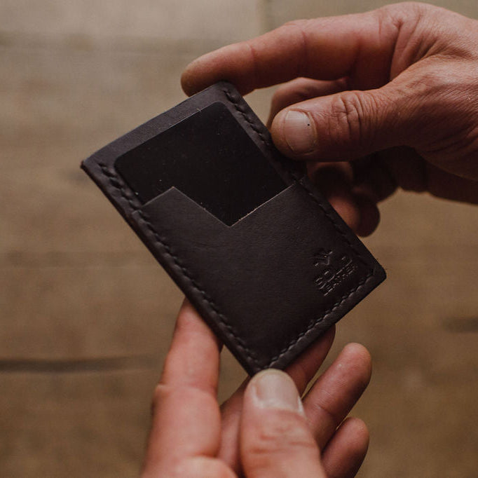 a dark brown Solid Leather minimalist wallet being held by a mans hands and a blurred background