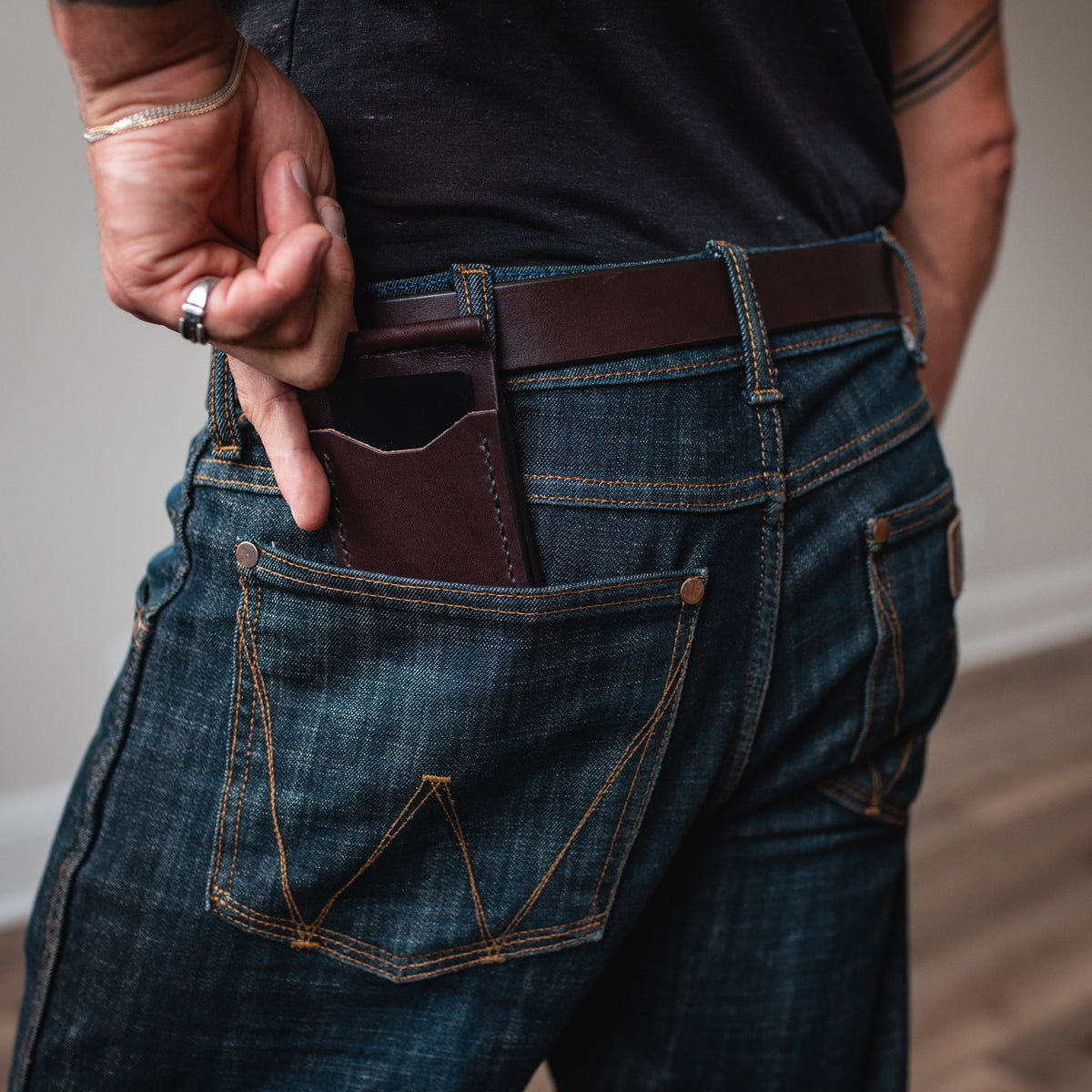 a dark brown full-grain leather money clip wallet in the back pocket of blue jeans with matching full grain brown leather belt.  Handmade by Solid Leather in Peterborough Ontario Canada