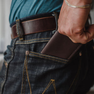 a Dark brown leather bifold cardholder wallet inserted into the back pocket of dark jeans with a matching dark brown Solid Leather belt 