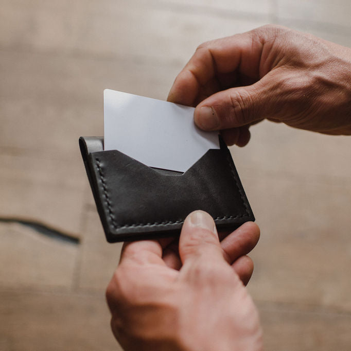 black solid leather bifold wallet with a white card held by mans hands. Handmade in Peterborough Ontario Canada by jesse bateson 