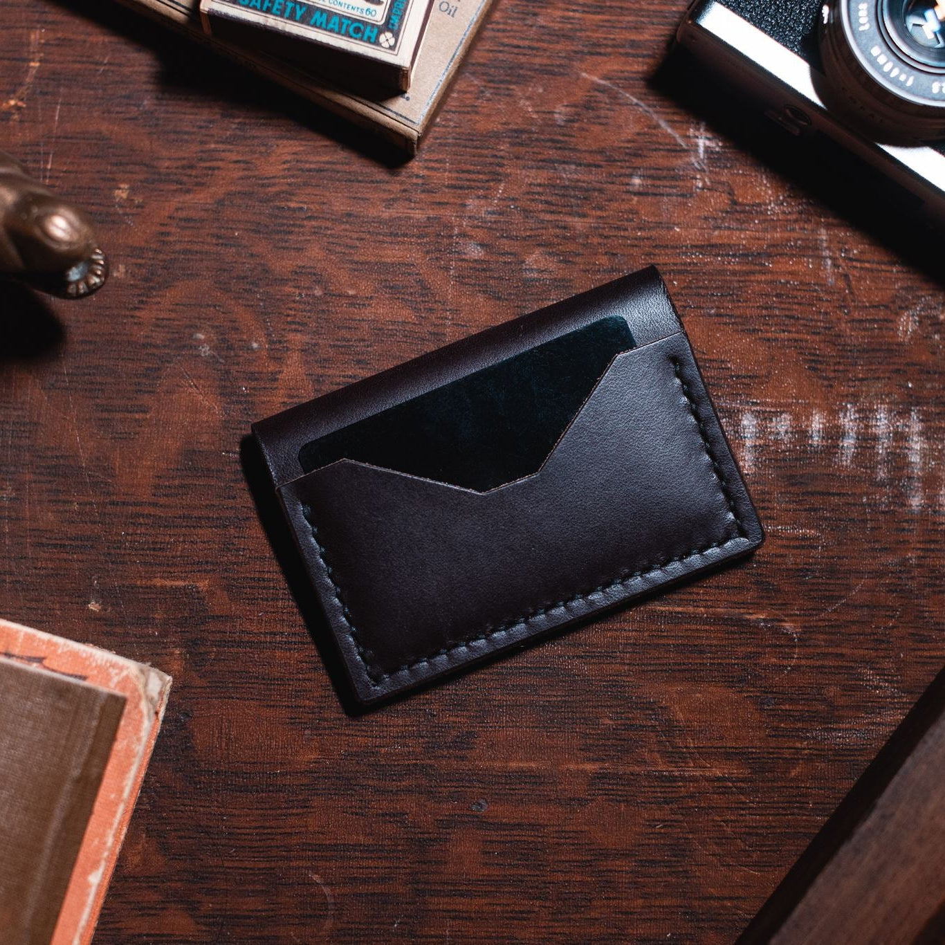 a dark brown leather bifold cardholder wallet on a dark wooden desk. Handmade in Peterborough Ontario by Jesse Bateson of Solid Leather 