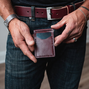 a burgundy full grain leather money clip wallet held by two hands with matching full grain leather belt and blue jeans 