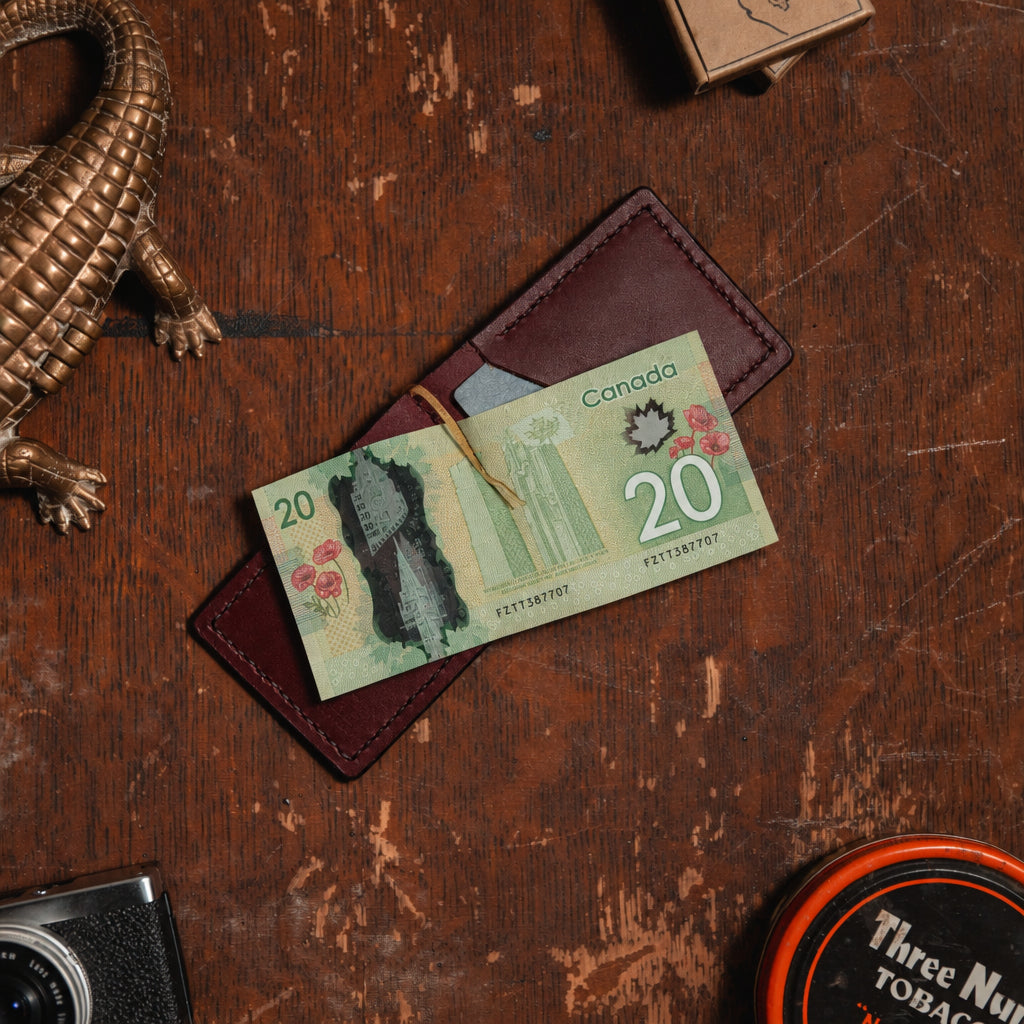 an open burgundy leather money clip wallet showing a $20 Canadian banknote on a wooden desk with vintage props 