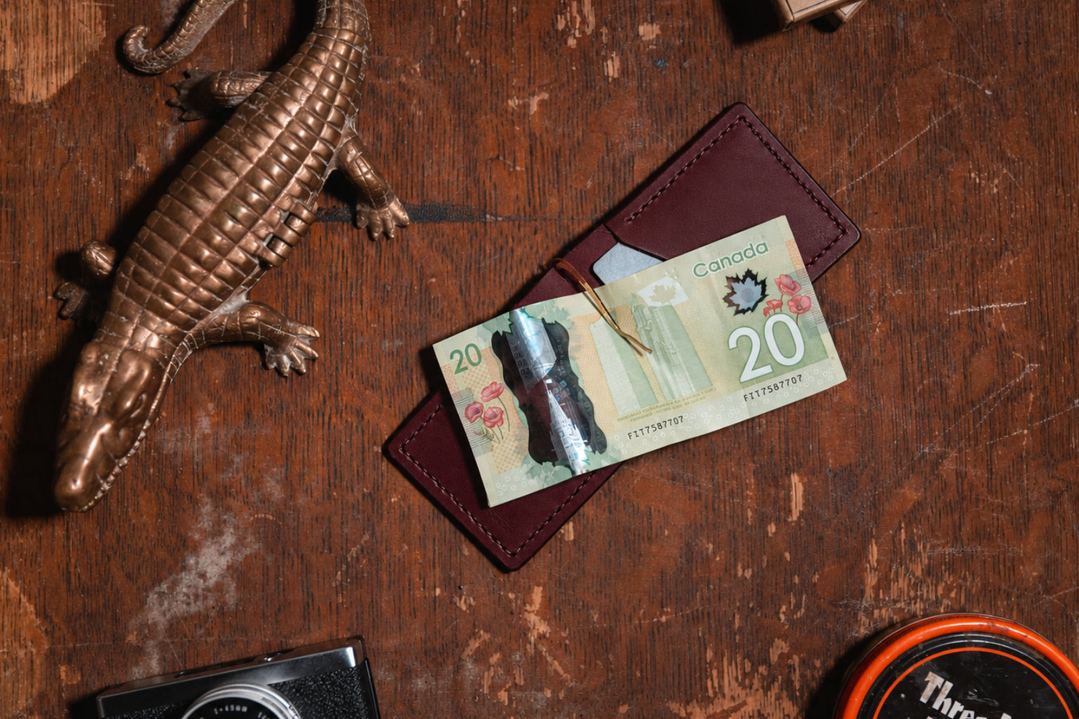 an open burgundy leather money clip wallet with $20 Canadian banknote shown on a wooden table with vintage props
