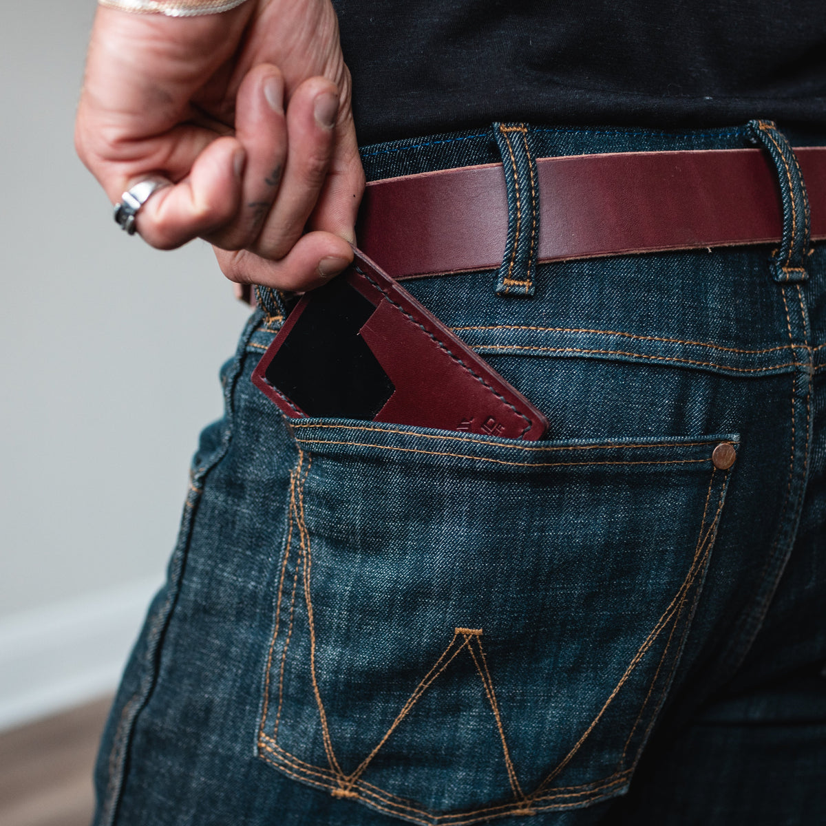 a burgundy leather slim cardholder wallet sits in the back pocket of jeans with a matching full-grain leather belt 