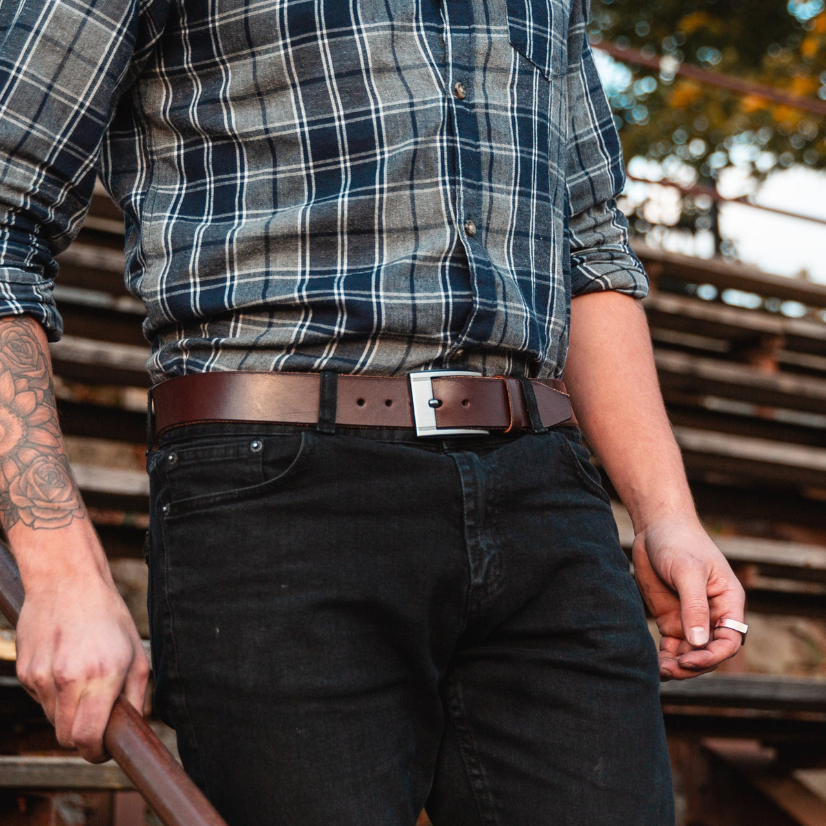 a dark brown full grain leather belt on a pair of dark jeans with a blurry warm background 
