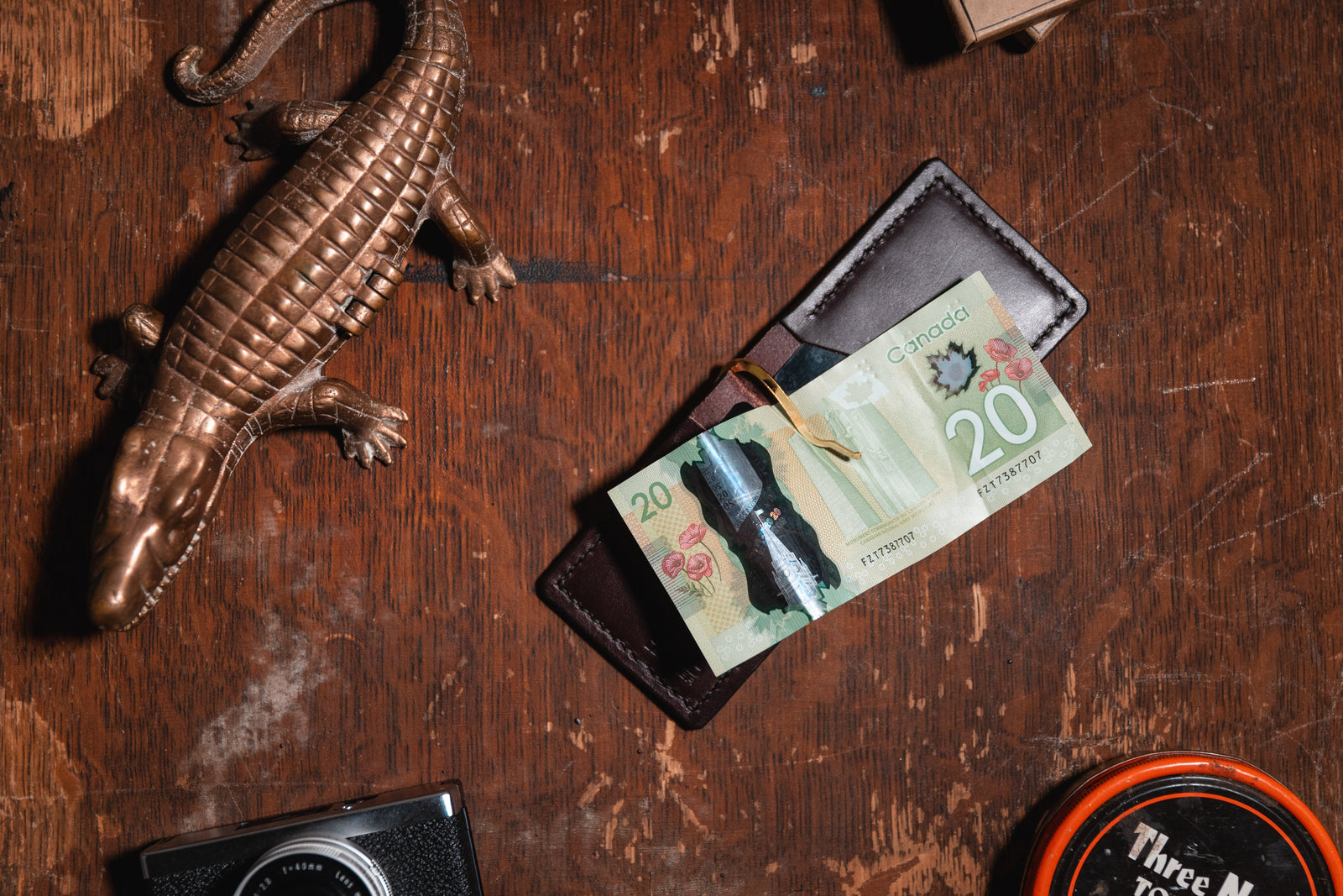an open dark brown leather money clip wallet with $20 Canadian banknote shown on a wooden table with vintage props