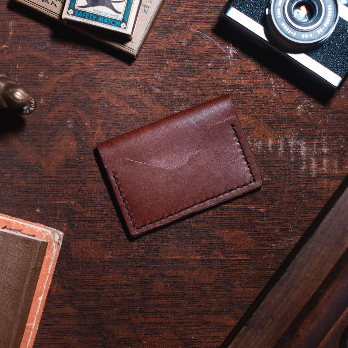 a Solid Leather bifold cardholder wallet in cognac brown leather on a dark wooden desk