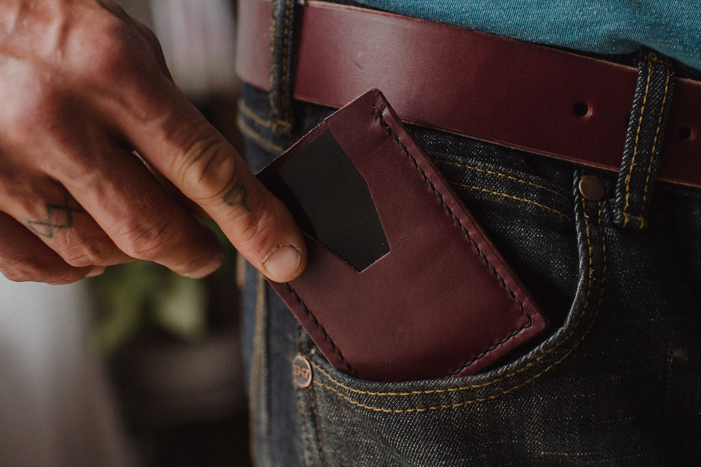 a minimalist cardholder wallet in burgundy leather sliding out of dark jeans 